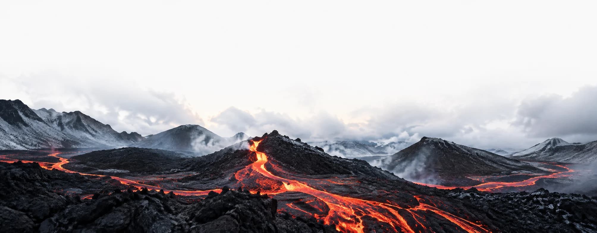 Dark volcanic mountains crossed by contained lava flows beneath pale mist